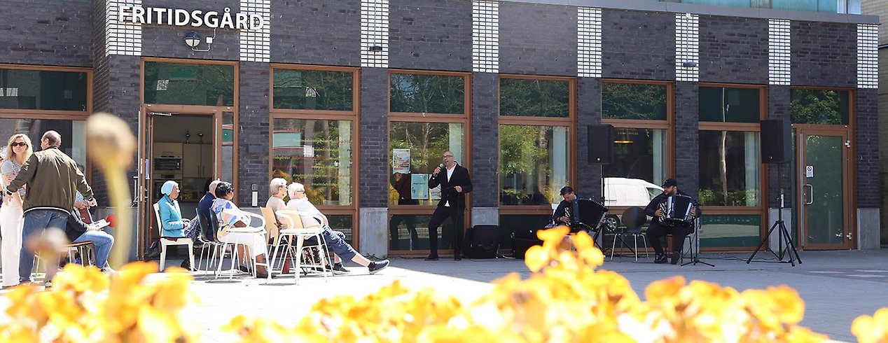 Fritidsgården i Holma, människor sitter utanför i solen och lyssnar på musik.