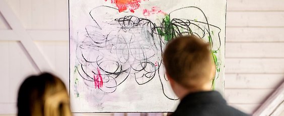 Två personer tittar på en tavla som hänger på en vägg