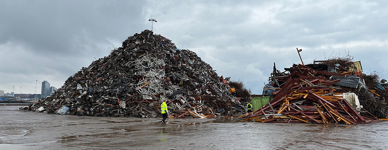 En inspektör står på ett industriområde med en stor hög avfall i bakgrunden.